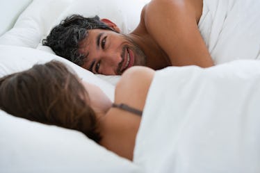 A couple lying in bed talking to one another while wrapped in blankets