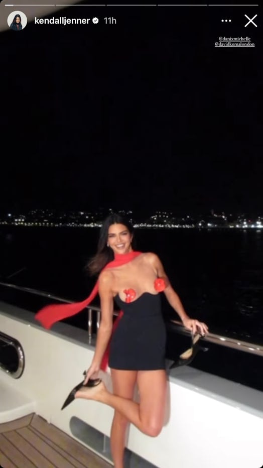 Kendall Jenner poses on a yacht wearing a black bodycon dress with red flowers as nipple pasties. 