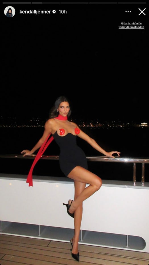 Kendall Jenner poses on a yacht wearing a black bodycon dress with red flowers as nipple pasties. 
