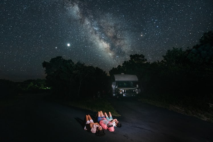 A family on an RV trip stargazes at night, lying on their backs and staring up at the night sky.