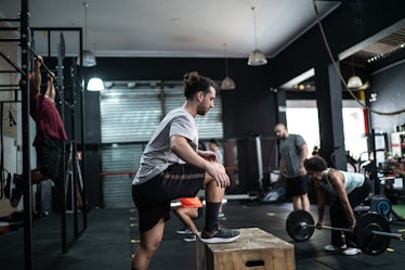 Men working out a gym. A man in the forefront does a box jump workout.
