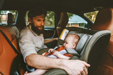 A dad putting his baby into a rear-facing carseat.
