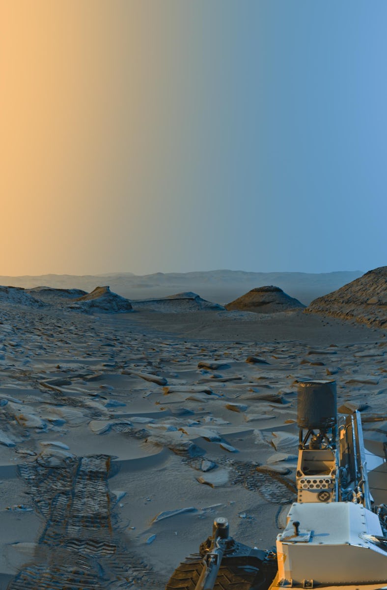 color image of a valley on Mars, with yellow sky on the left and blue sky on the right, and a rover ...