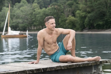 A man in swim trunks sitting on a lake pier.