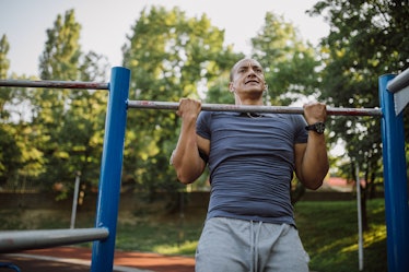 A man doing pull-ups on a playground outdoors.