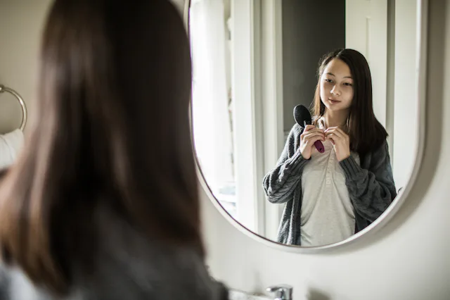 A teen looks at their body in the mirror.