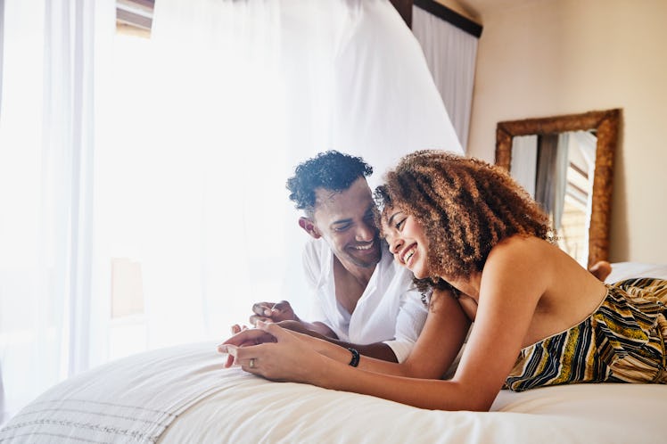 Happy couple laying on their stomachs in bed smiling and talking