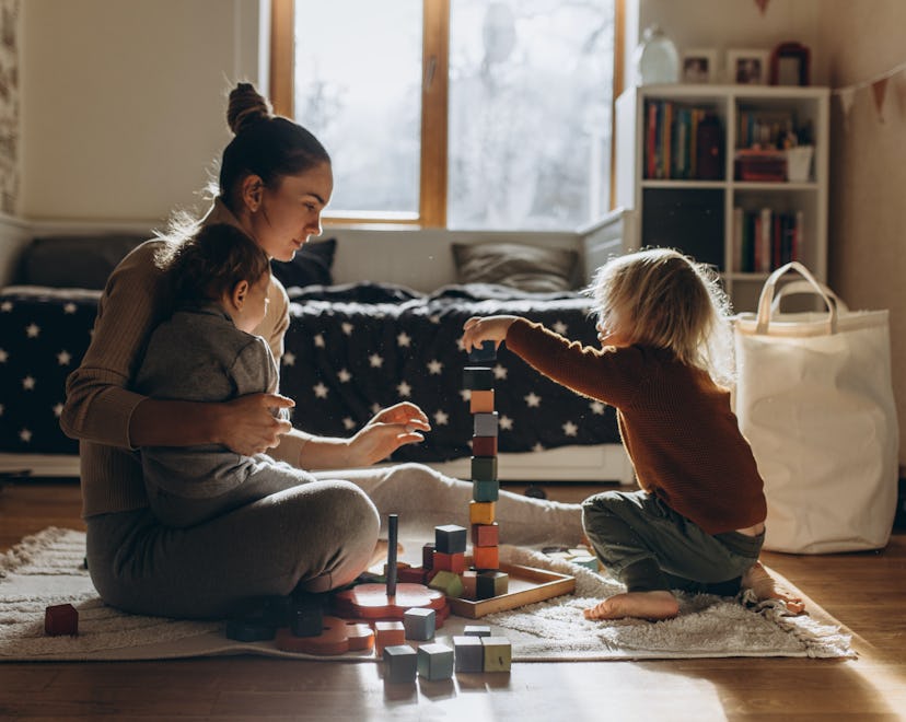 Young Mother playing with children while sitting on floor at home with wooden toys, what parents nee...