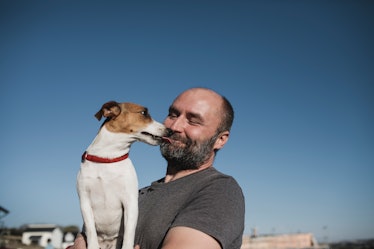 A man with a balding head outdoors, getting kisses from a dog.