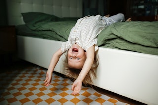 An energetic toddler hangs off the edge of the bed.