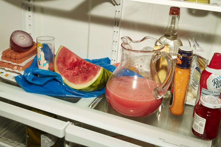 an open refrigerator containing a watermelon wedge and a pitcher of watermelon juice, among other co...