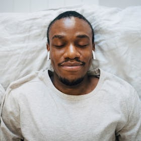 A man lying in bed, relaxing with his eyes closed, as he tries autogenic training.