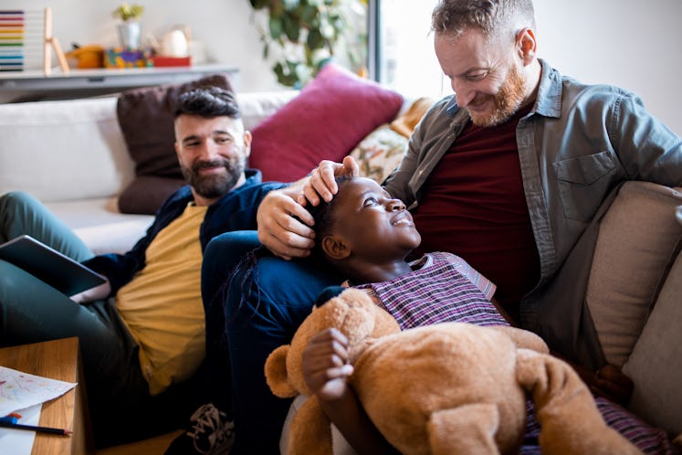 Two dads on a couch with their son, smiling.