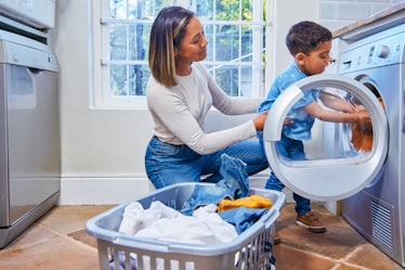 A boy helps his mom take laundry out of the laundry machine.