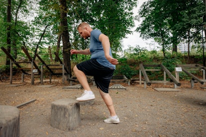 A man doing step-ups at a park on a tree stump.