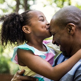 A girl kissing her bald father's head.