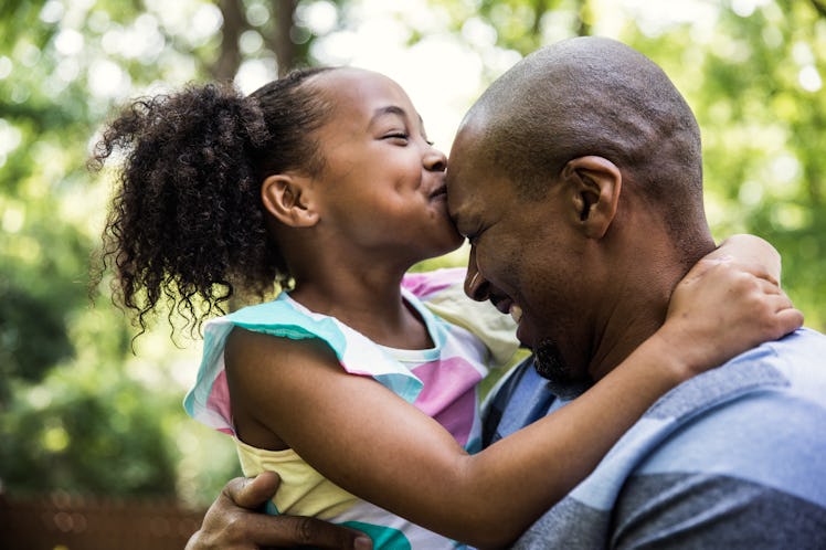 A girl kissing her bald father's head.