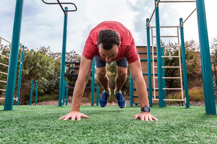 A man doing burpees on a playground outdoors.
