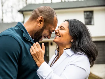 A couple laughing and embracing outside of their house.