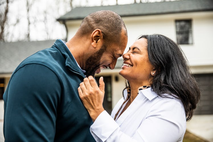 A couple laughing and embracing outside of their house.