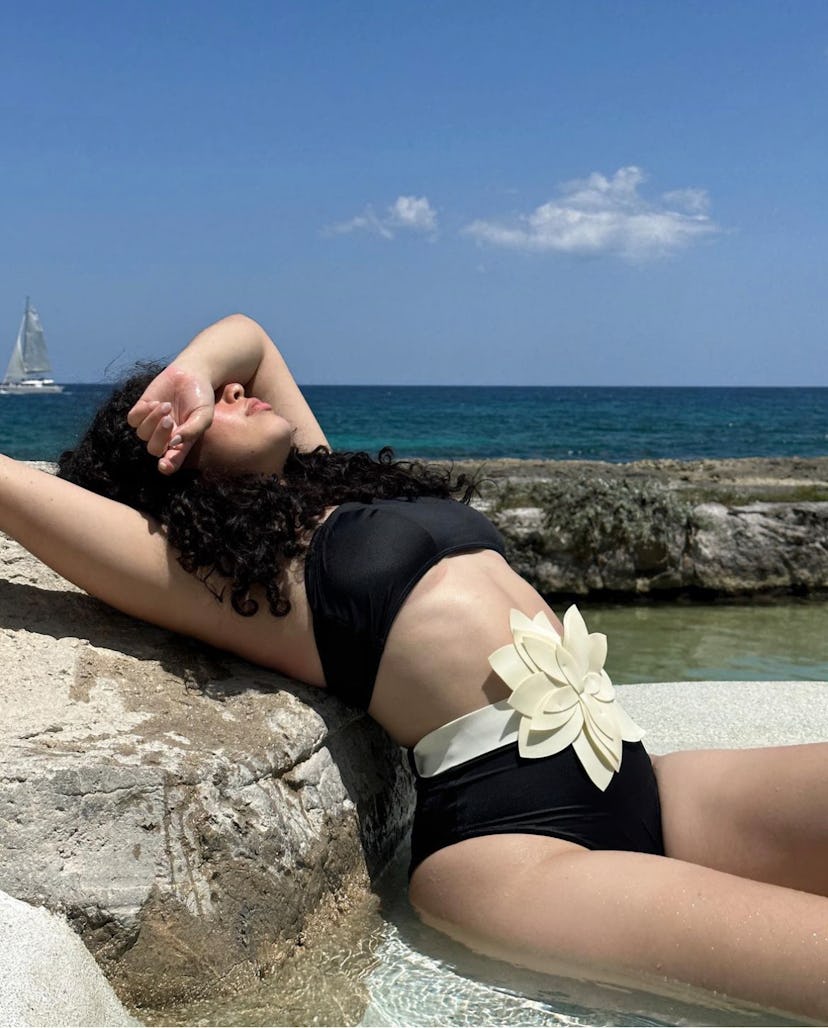 woman on beach and rocks lies in the sun with harm over head and bikini 