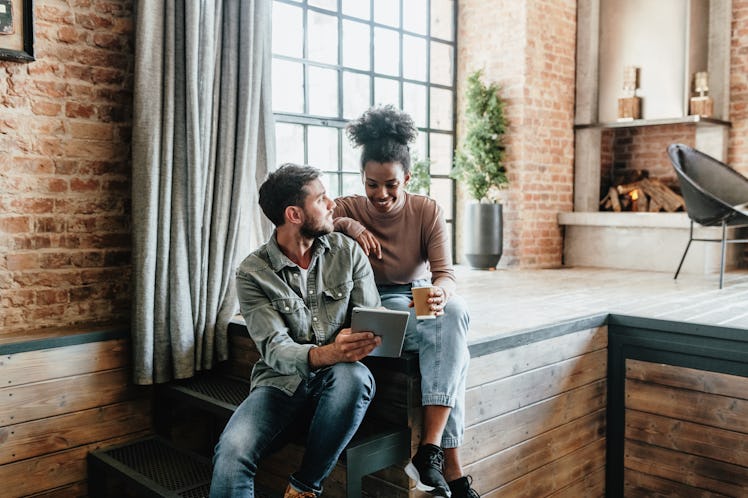 Couple talking and sipping beer near window in apartment