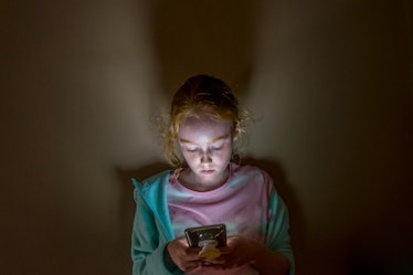 A child looking at their cell phone in the dark.