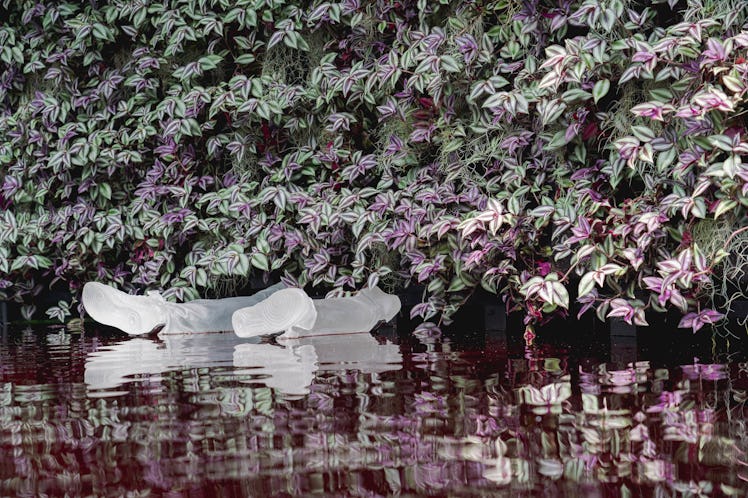 a sculpture of white glass legs peek out beneath a shrub.