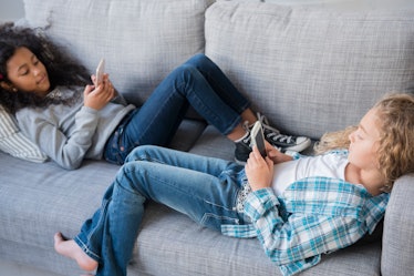 Two kids lying on a sofa, on their phones.