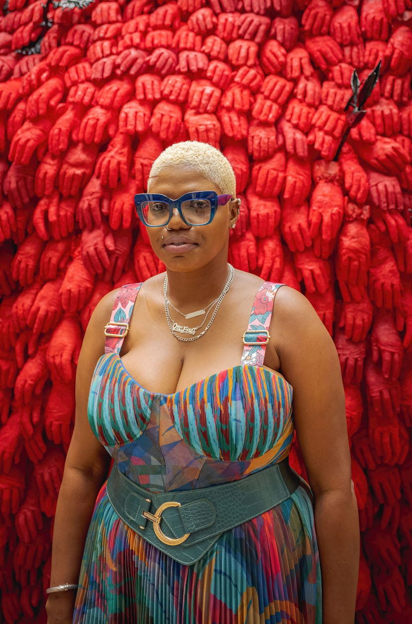 the artist Ebony G. Patterson in front of a sculpture made of red gloved hands titled "...fester..."...