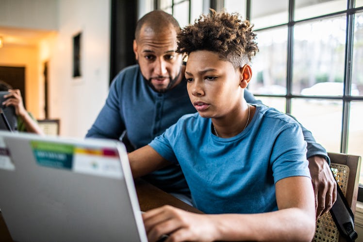 A dad helping his son do homework on a laptop.