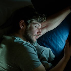 A man on his phone at night in bed.