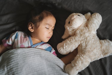 A toddler sleeping in bed with a stuffed animal.