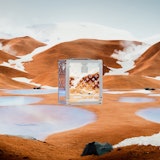 A  clear, lucite Louis Vuitton trunk floating in a sandy, mountainous setting