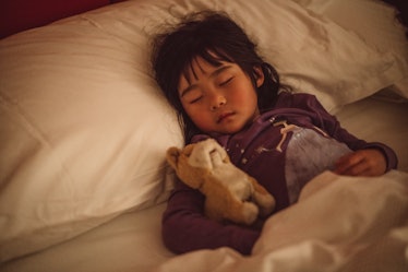 A child sleeping in bed with a stuffed animal.