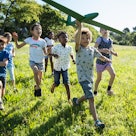 A group of children running through a field with a model airplane.