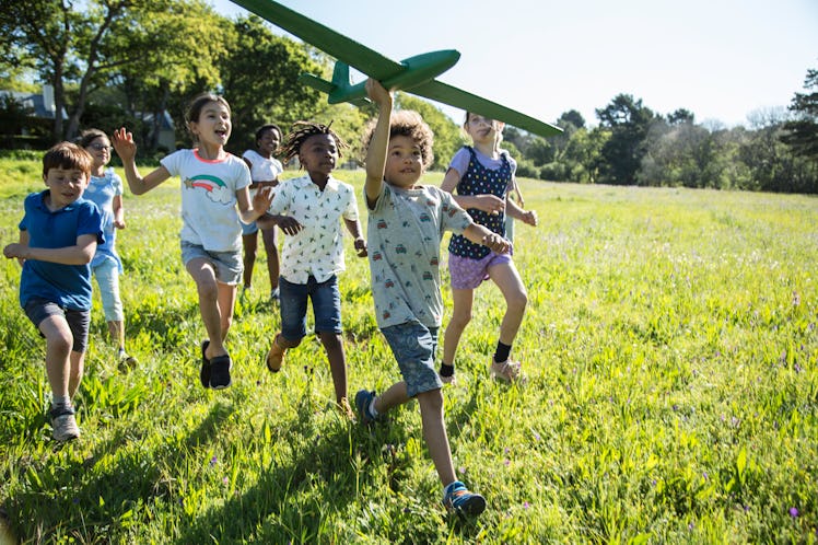 A group of children running through a field with a model airplane.