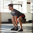A man doing kettlebell squats at a gym.