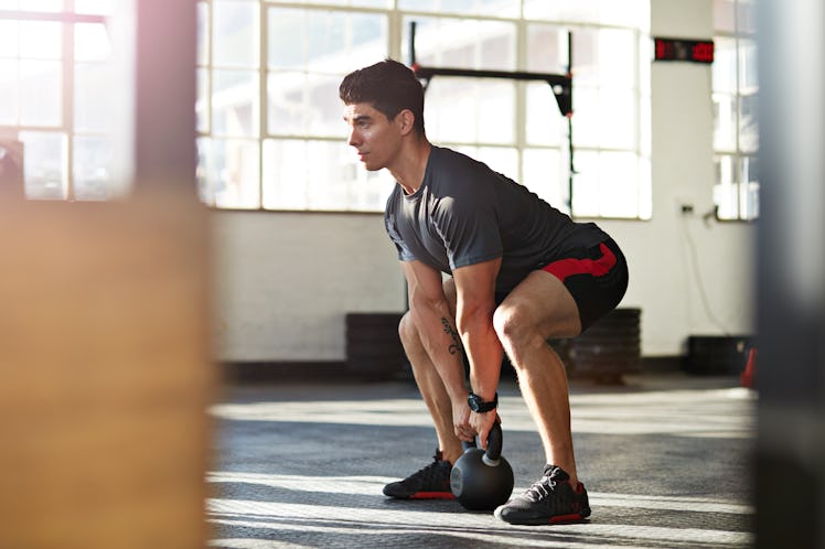 A man doing kettlebell squats at a gym.