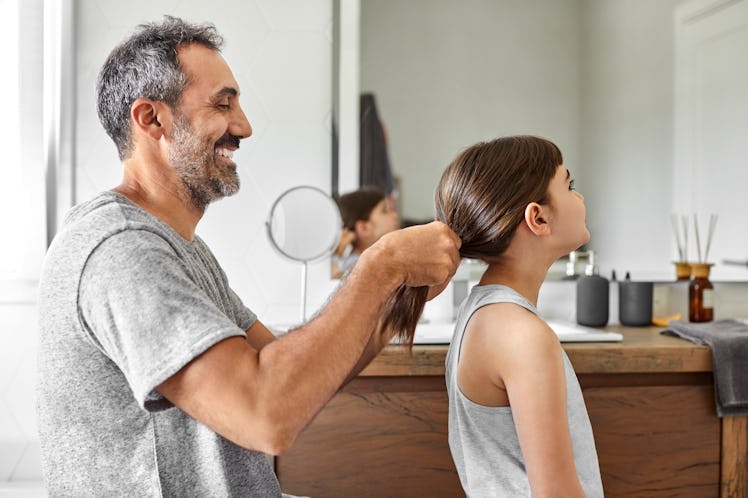 A smiling dad putting his daughter's hair up in a ponytail