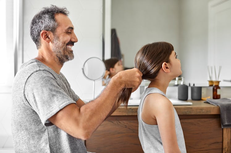 A smiling dad putting his daughter's hair up in a ponytail