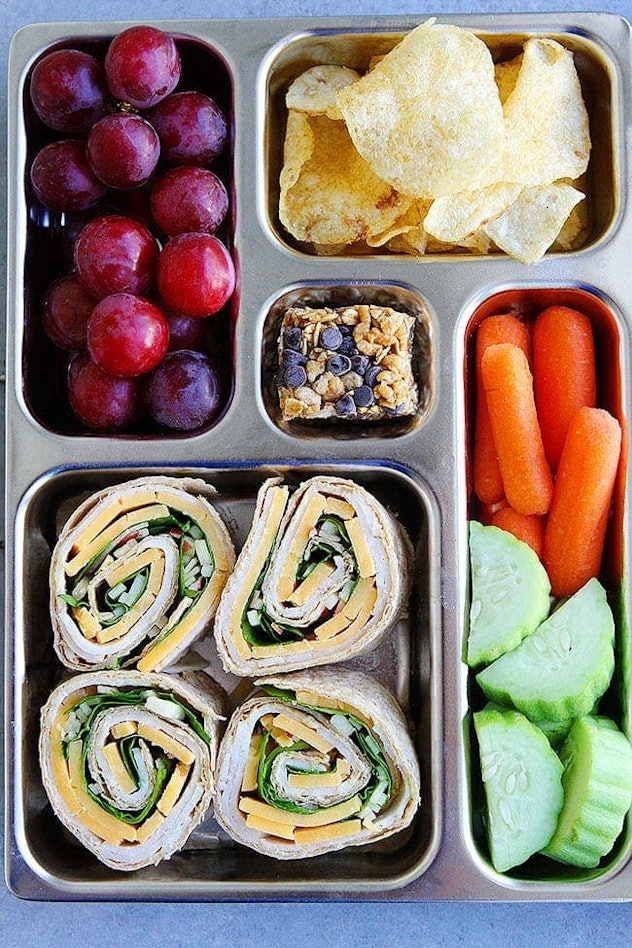 A nutritious school lunch idea: pinwheels, grapes, veggies, and granola.