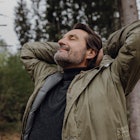 A man stretching, breathing deeply while on a nature walk.