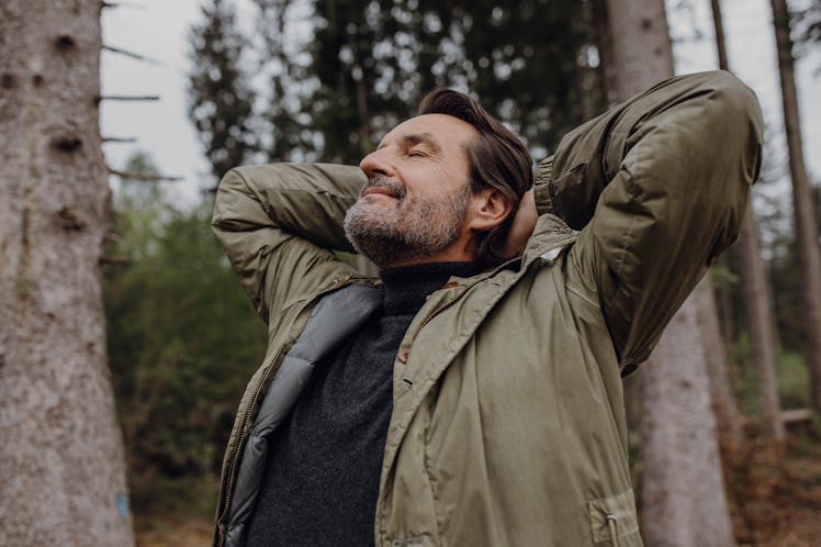 A man stretching, breathing deeply while on a nature walk.