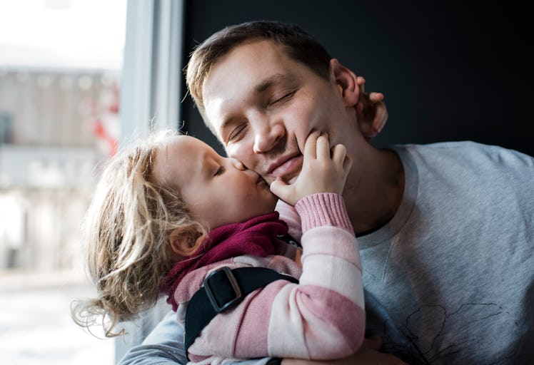An overly affectionate child pulls at her dad's face and kisses her father on the cheek.
