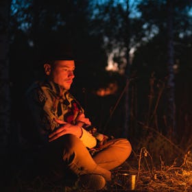 A man staring into a bonfire outside at night.