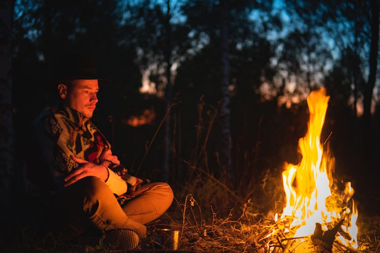 A man staring into a bonfire outside at night.