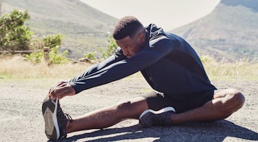 A man outdoors, sitting and stretching his hamstrings and calves.