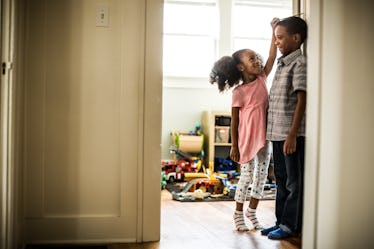 A sister measures her brother's height against a wall.