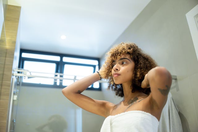 A woman looks in the mirror with her armpits exposed.